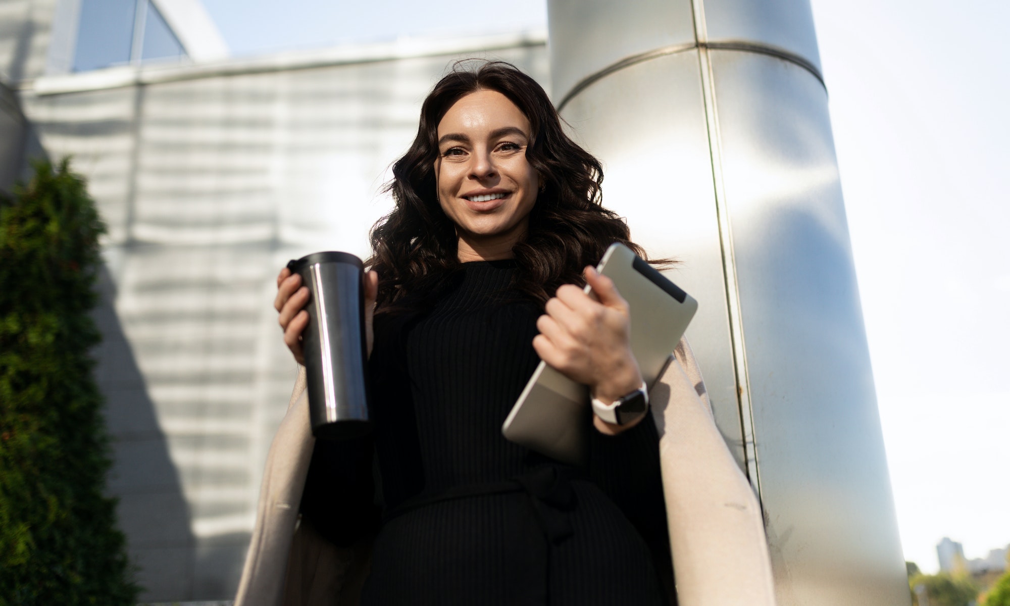 happy young adult woman student with thermo mug and tablet on university background